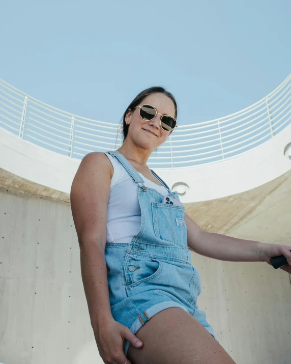 a woman standing outside in her jean overall shorts and sun glasses