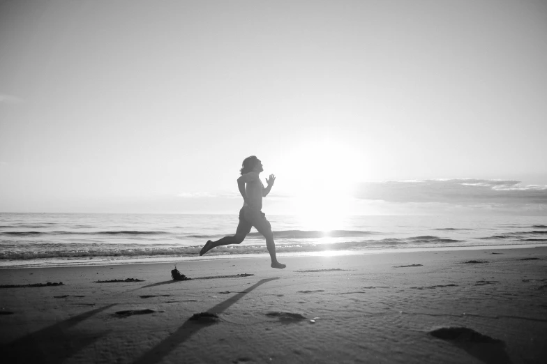 a woman running along the beach in front of the sun