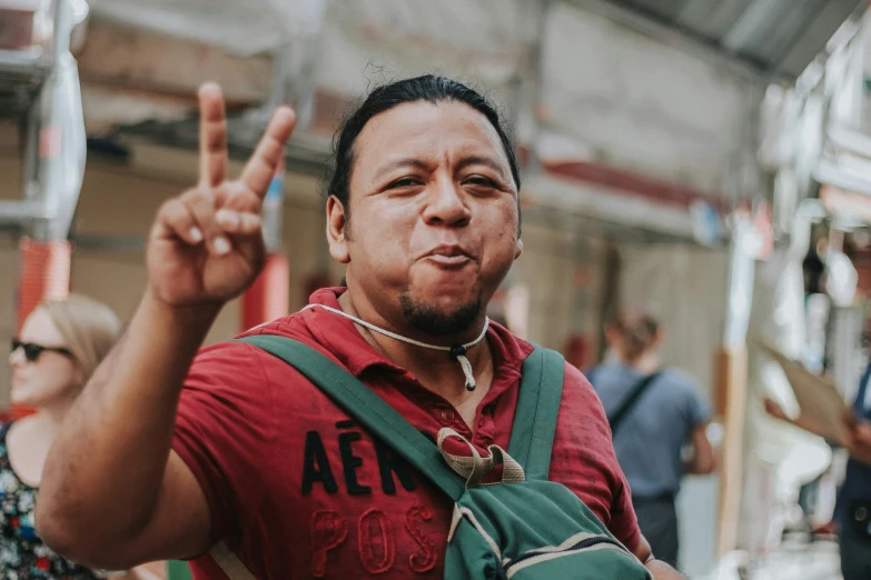 a man wearing a green backpack making a peace sign