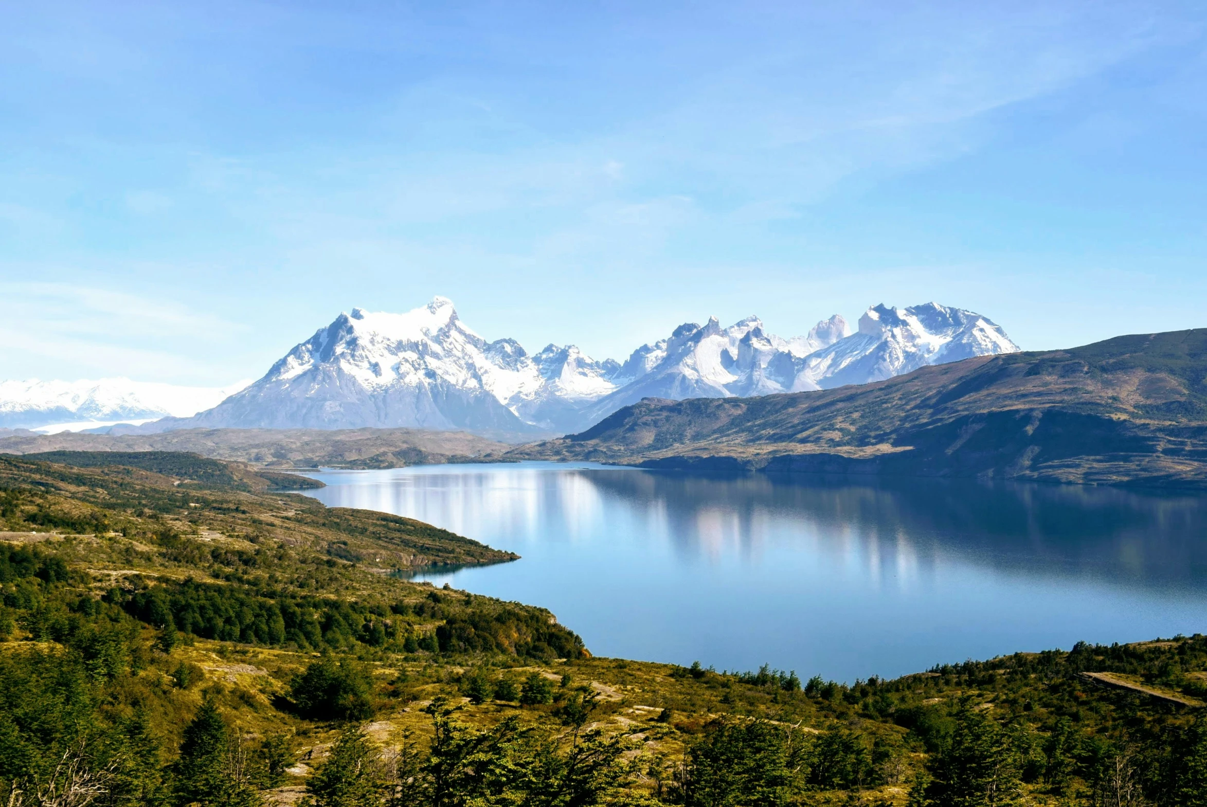 a mountain range has snow capped peaks over a lake