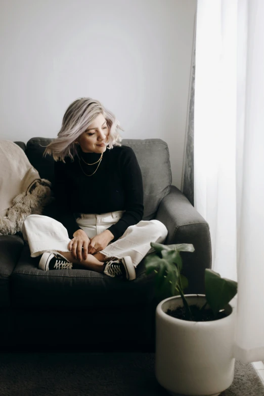 a woman with a gray hair sits on a sofa in front of a window