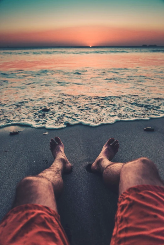 a pair of feet wearing red shorts standing in the sand of a beach