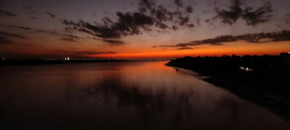 a sunset on the ocean with clouds and bridge in the background