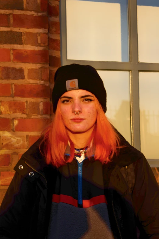 the young woman has bright orange hair and is wearing a black hat
