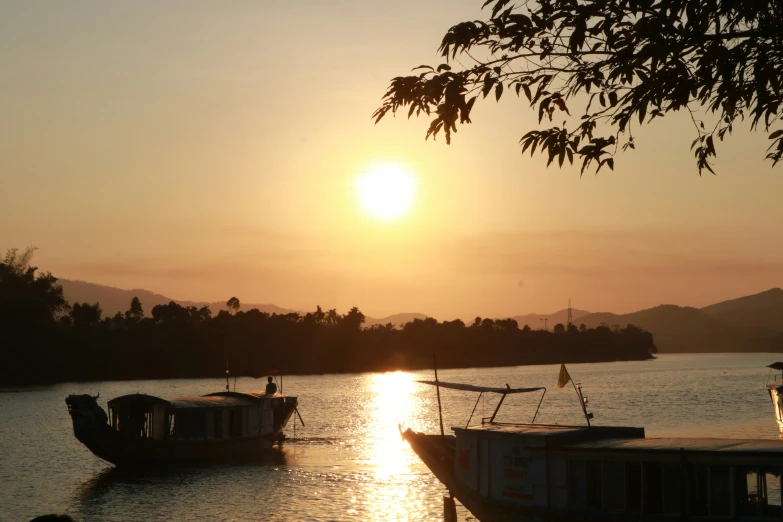 two boats floating in a river at sunset