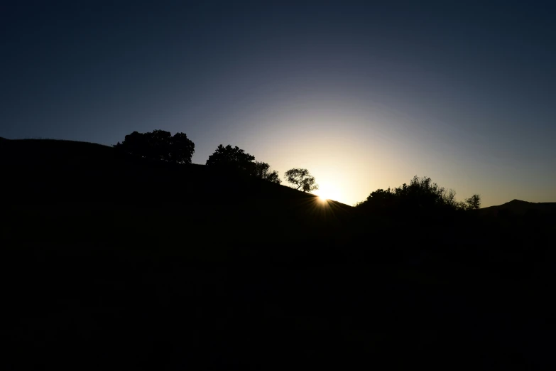 the sun is setting over trees on the hillside