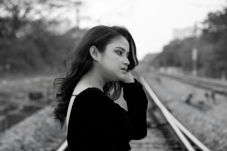 a woman standing alone on train tracks looking off into the distance