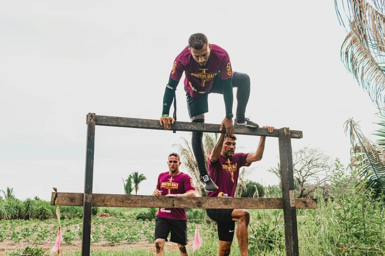 two young men in maroon shirts are climbing a wooden structure