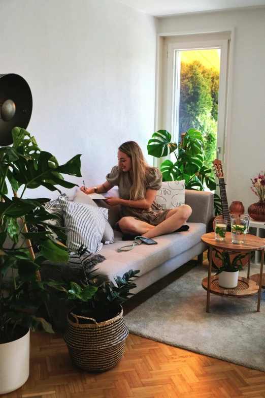 a girl sits on a couch surrounded by plants