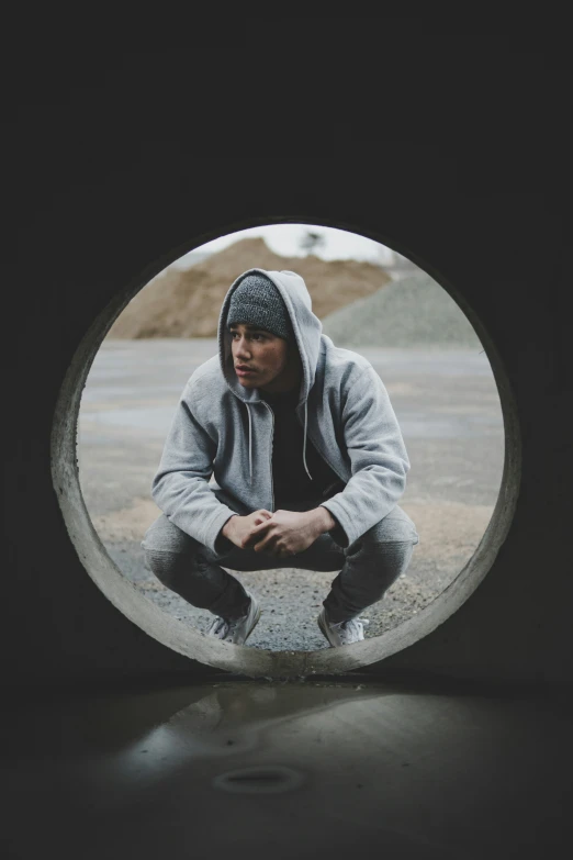 a man in a hooded sweatshirt looks out through a hole