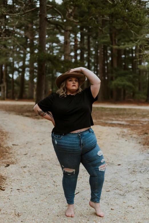 a woman in a black shirt and jeans is standing on the dirt road