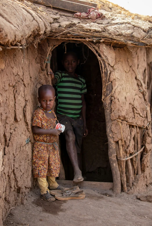 two small children are standing outside a clay building