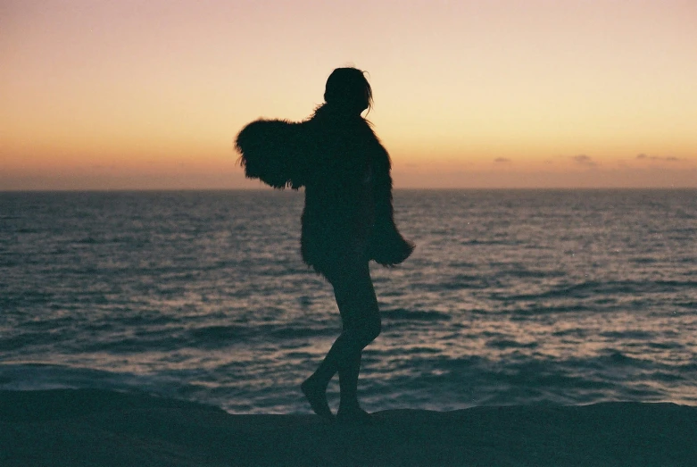 a woman is standing on the edge of a cliff, with a beautiful sunset in the background