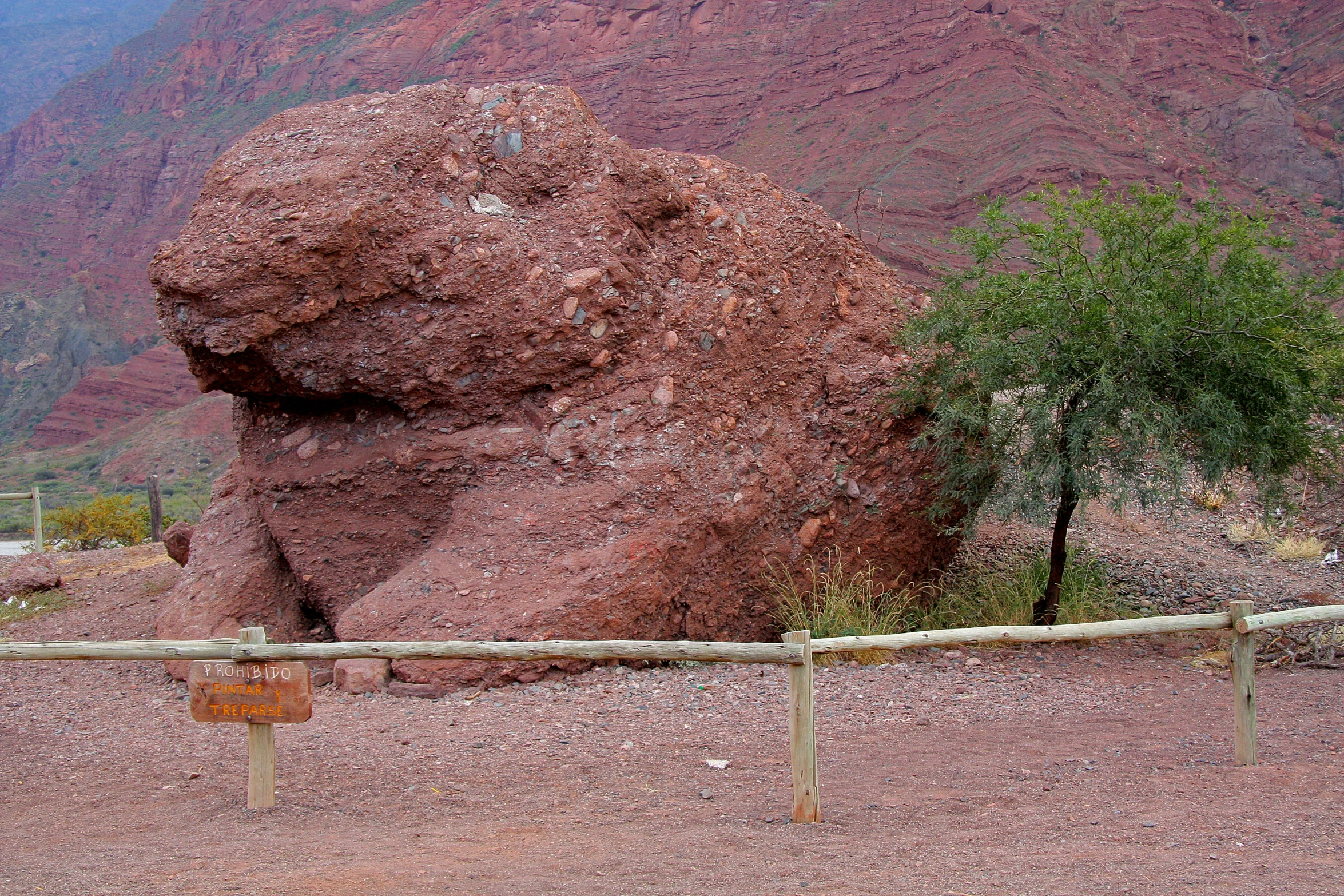 a large rock in the dirt near a fence