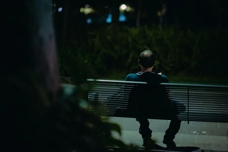a person sitting on a bench at night looking across the street