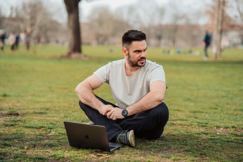 man squatting in the grass looking at laptop