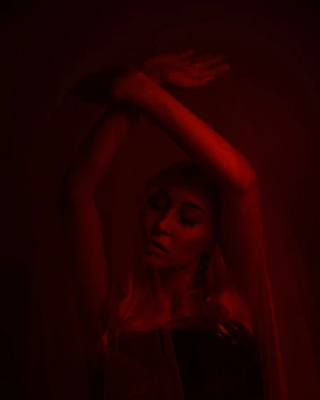 woman in red light under veil holding on to her arms
