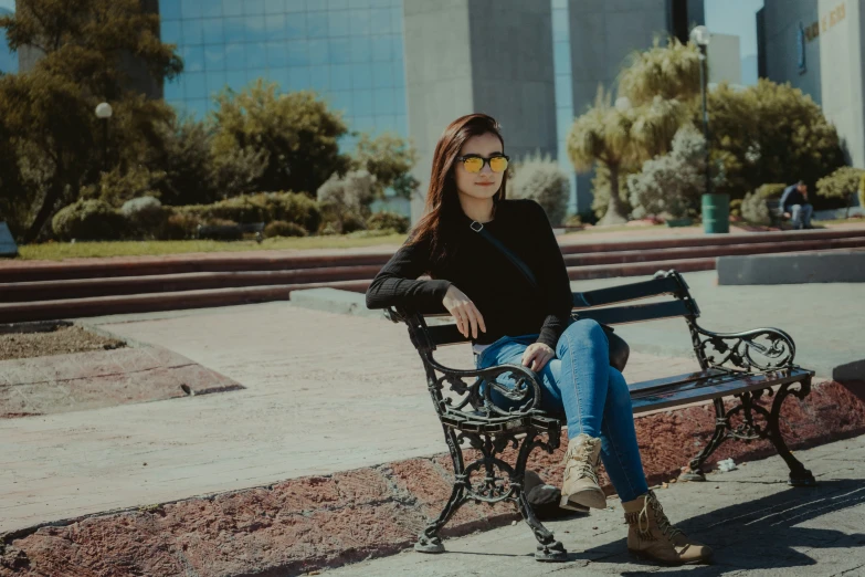 a woman sitting on a bench wearing black jacket and jeans