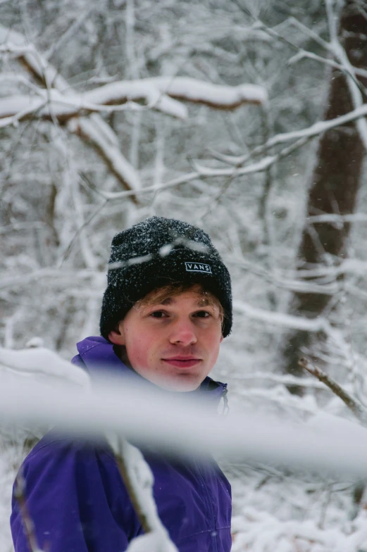 the young man in a winter hat is standing in the snow