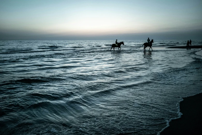 the silhouettes of people riding horses on the beach at sunrise