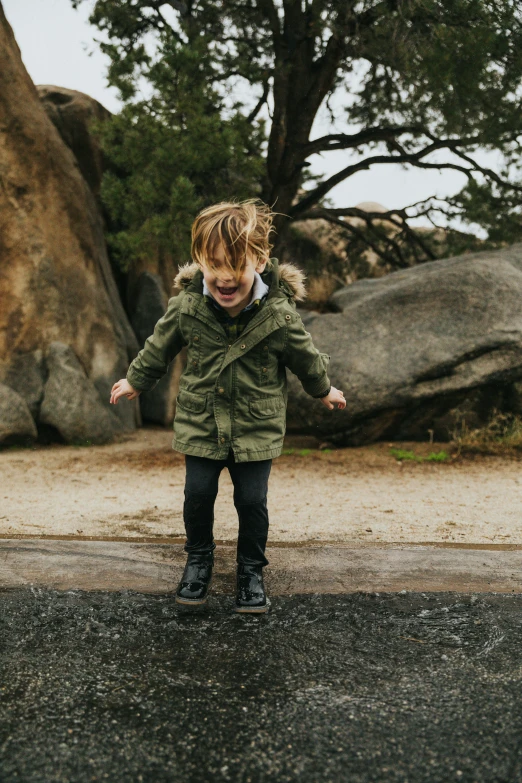 a little  standing on wet ground next to a tree