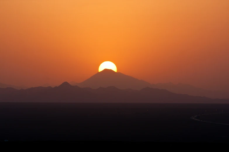 a setting sun behind a mountain silhouette with the horizon in the foreground