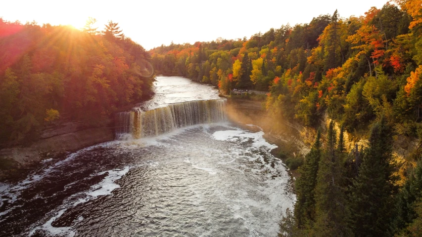 the sun setting over a water fall with fall trees