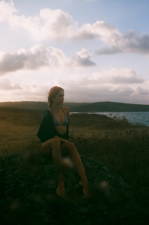 woman sitting on large rock near body of water