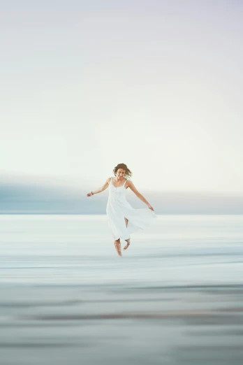 a woman in a white dress jumping across the water
