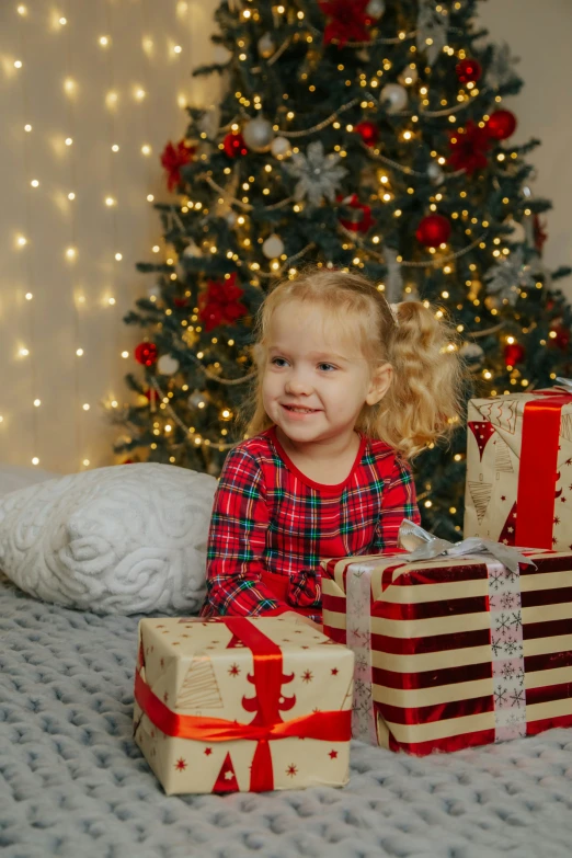 a little girl posing with christmas presents in front of her tree