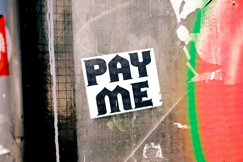 a pay me sticker attached to a wall near a pole