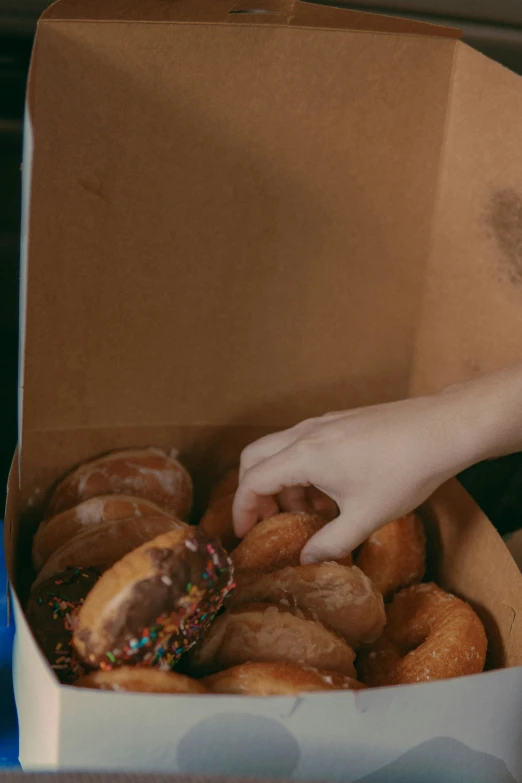 a hand picking up a donut out of a box