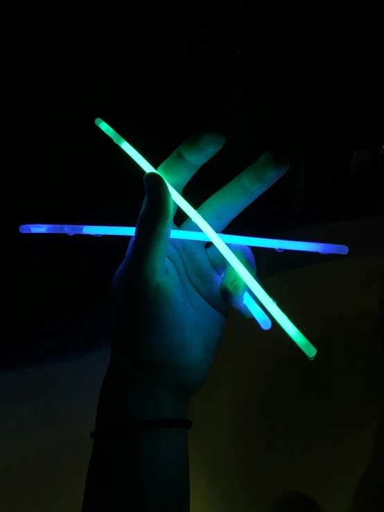 a hand holding onto two glowing plastic chopsticks