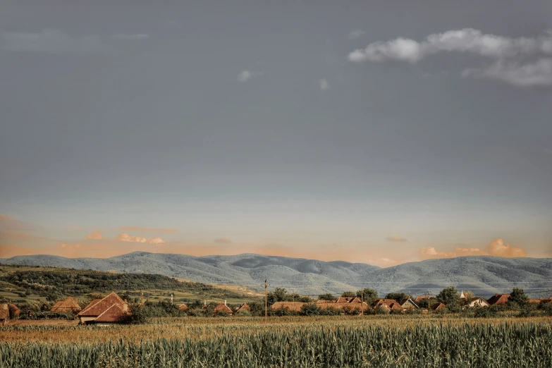 mountains rise in the distance behind a farm and grass field