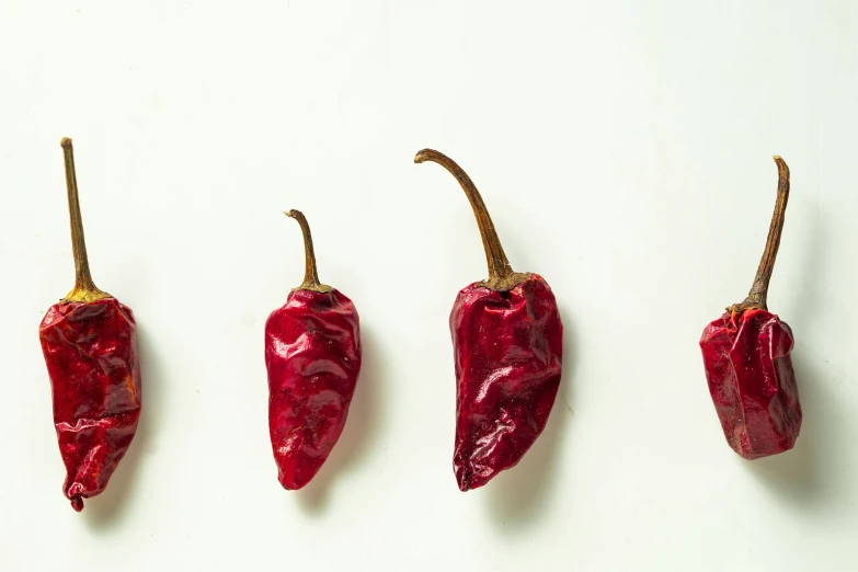 three small red peppers in a line against a white wall