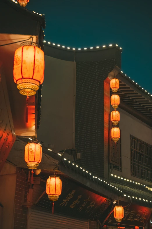 multiple lit chinese lanterns hanging outside on a building