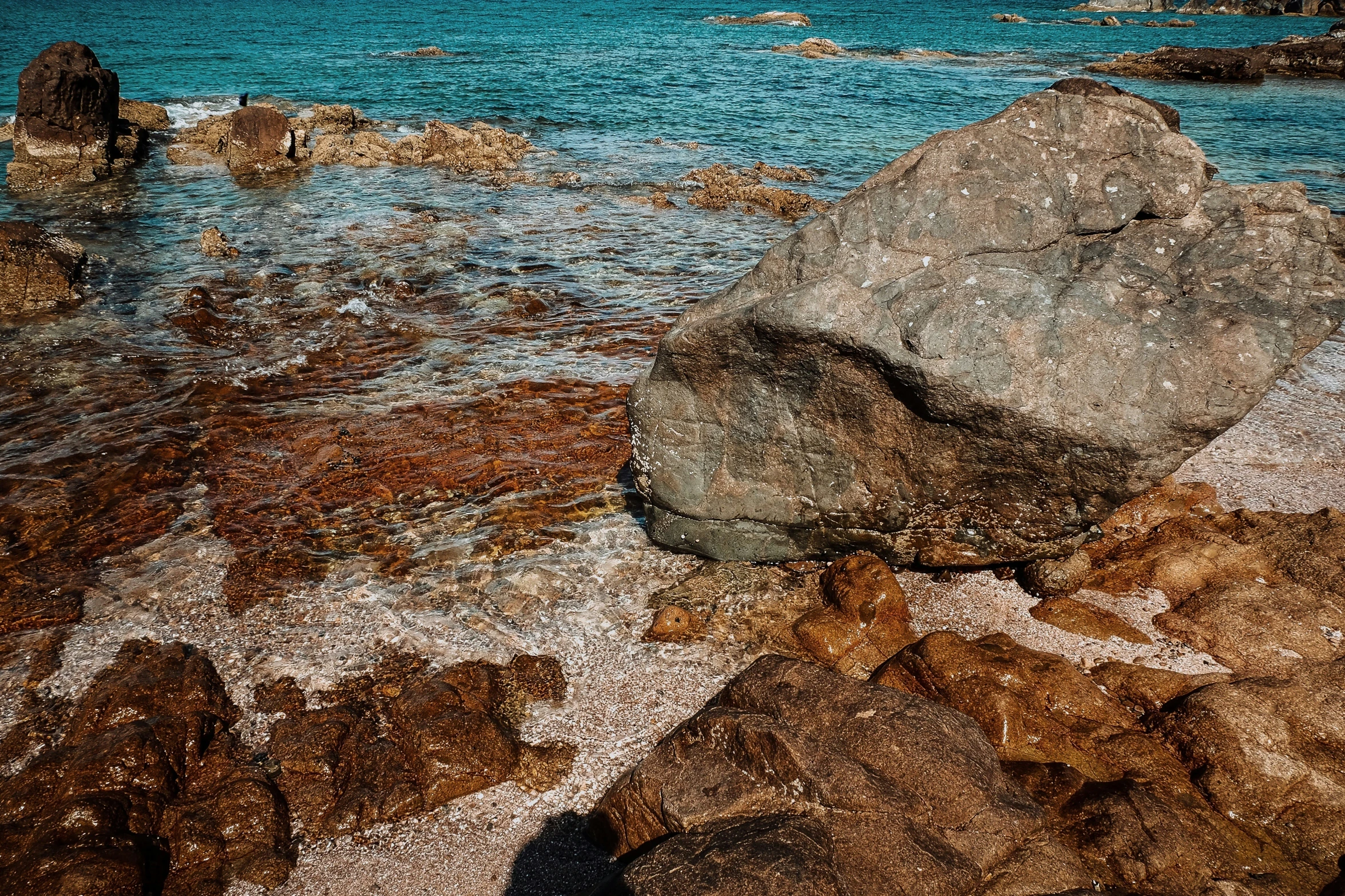 a bunch of rocks on some sand by the water