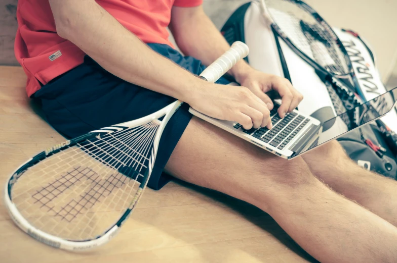 man with tennis racket and laptop on table