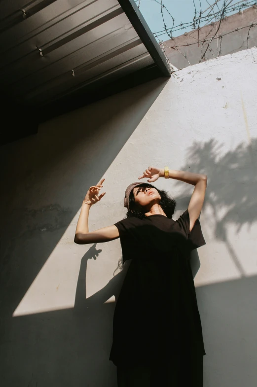 woman in a dark dress standing by wall with her arm on her head