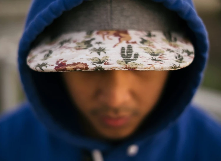 the young man is wearing a blue hoodie and is holding a patterned paper hat on his head