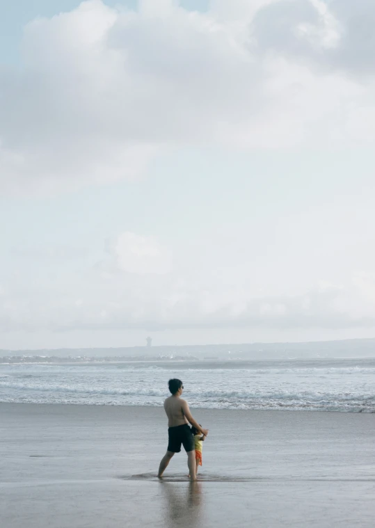 a man in black shorts walks along the beach