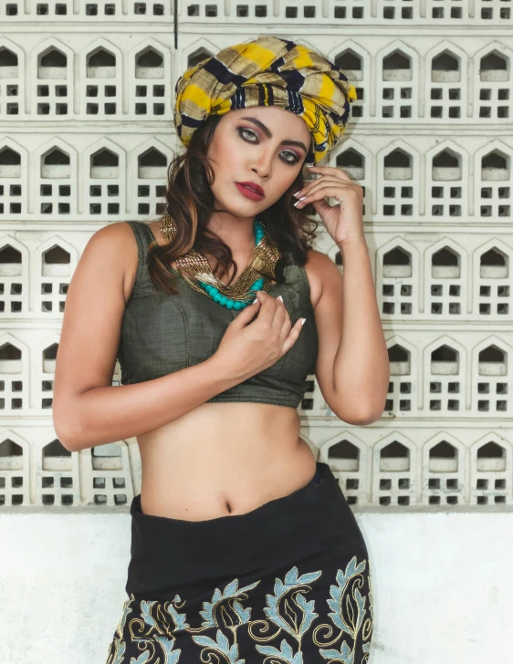 a woman with a patterned head scarf and head dress poses against a wall