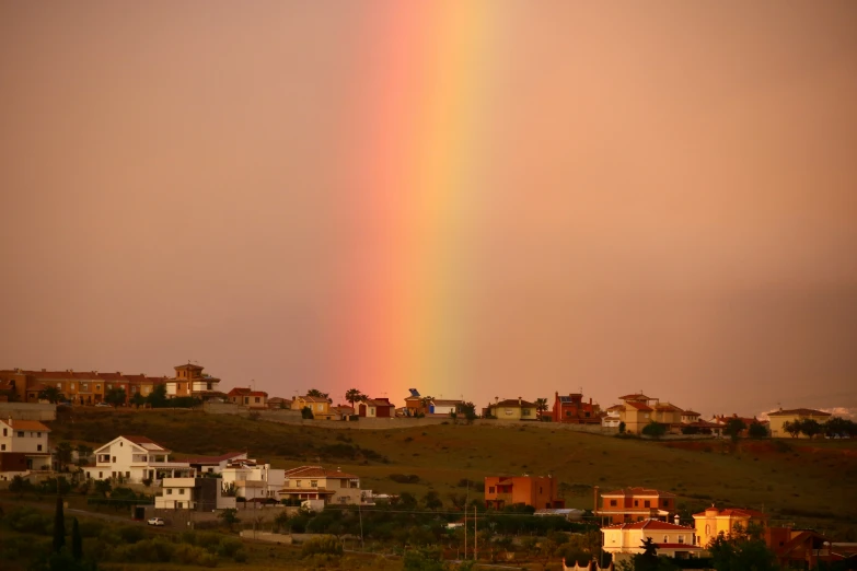 a rainbow shines above the hillside of a small town