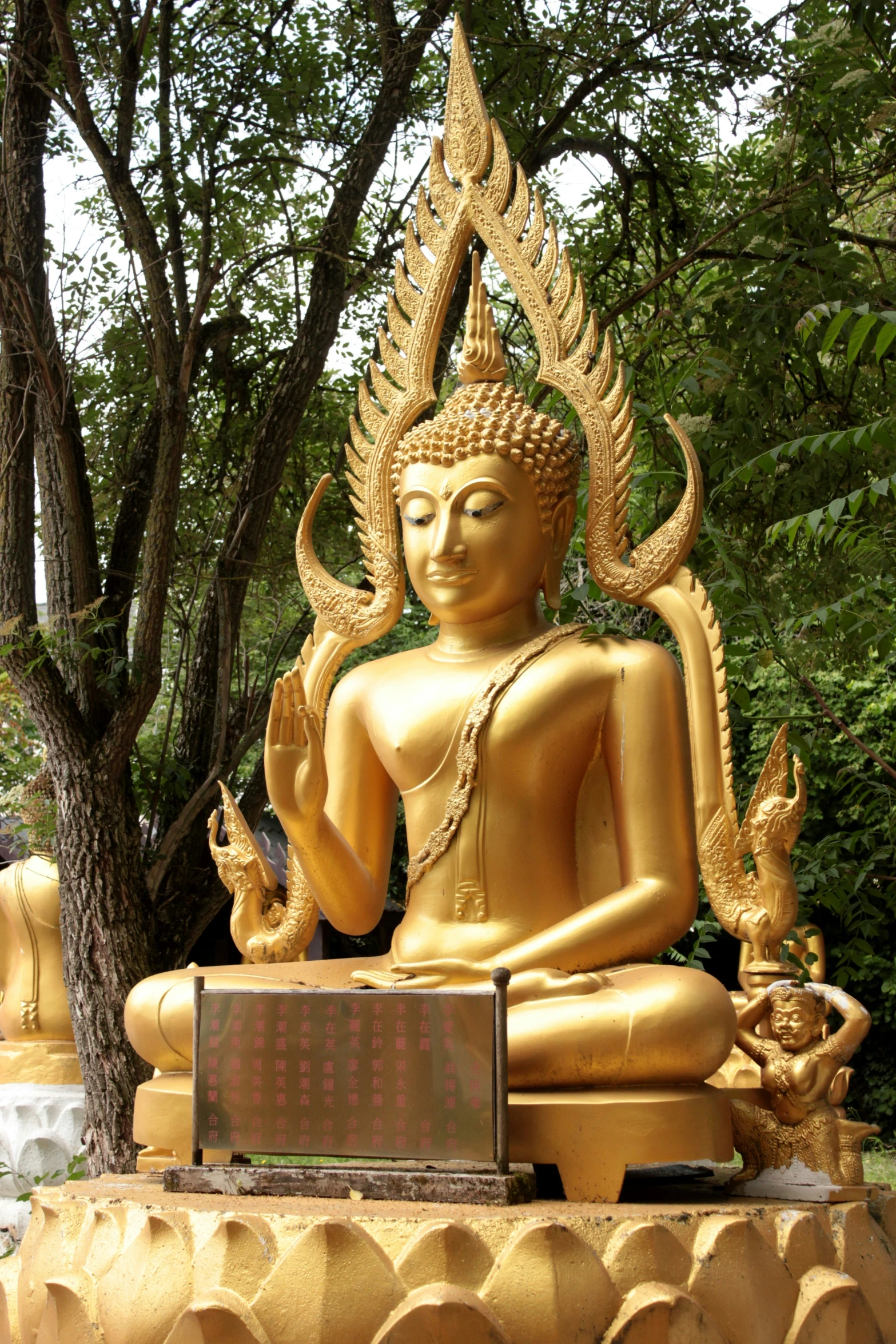 gold buddha statue sitting in the middle of a forest