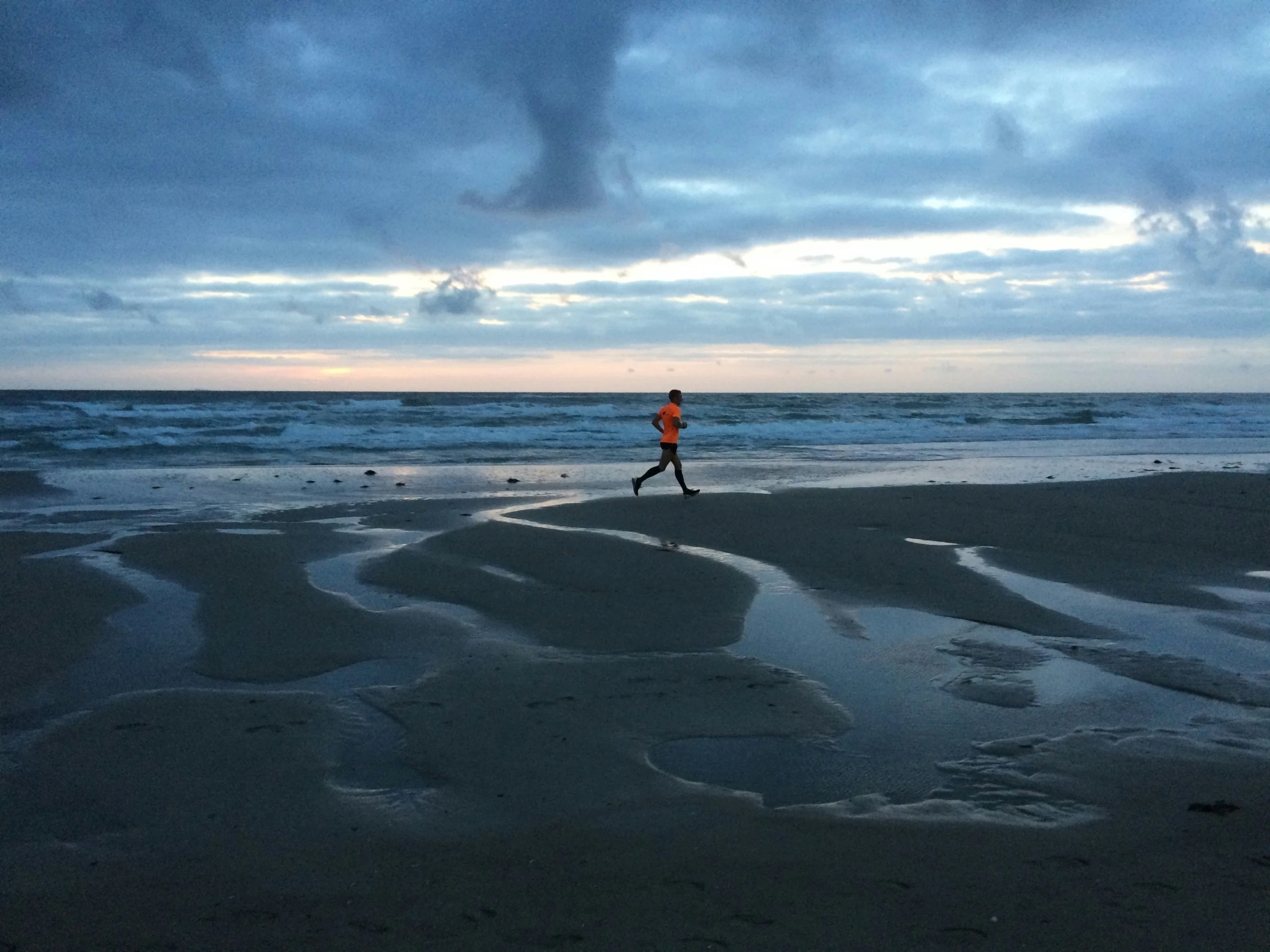 man running across beach with storm moving in the background