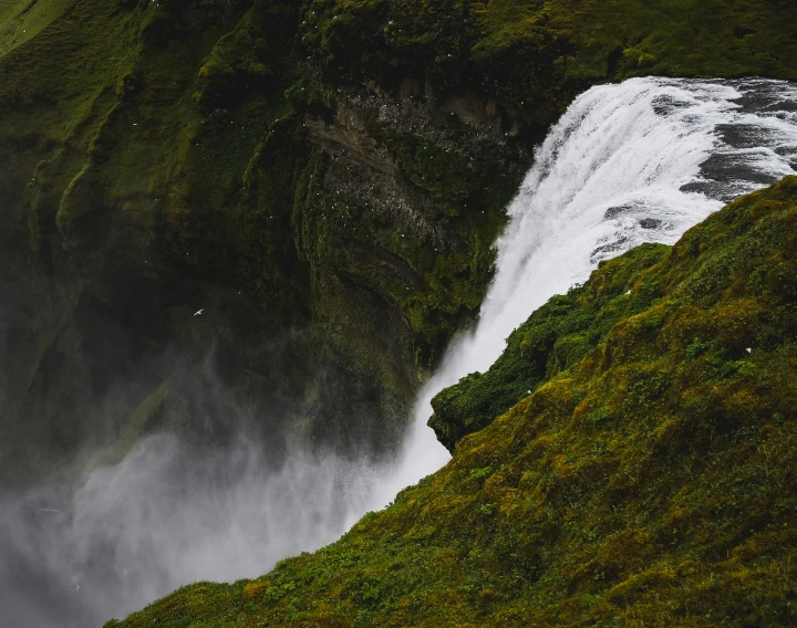 a waterfall surrounded by green grass near a body of water