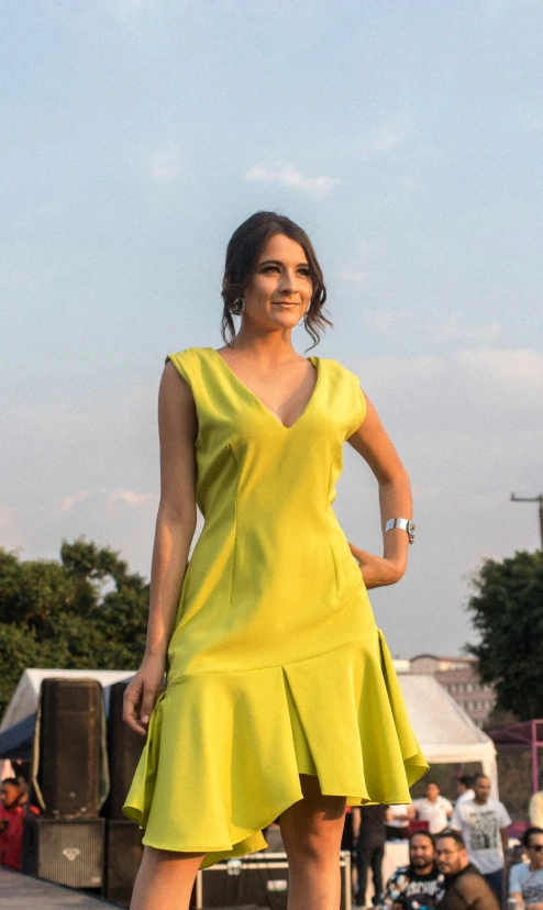 a young woman wearing a yellow dress, standing on a sidewalk with her foot up