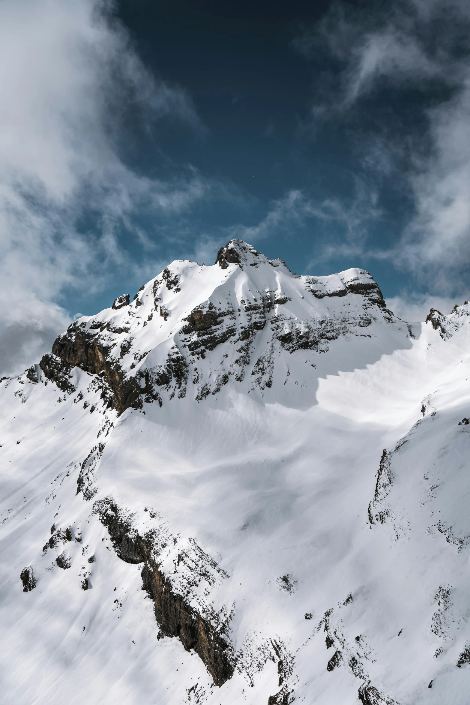 an expanse of snow covering the slopes and in front of a cloudy sky