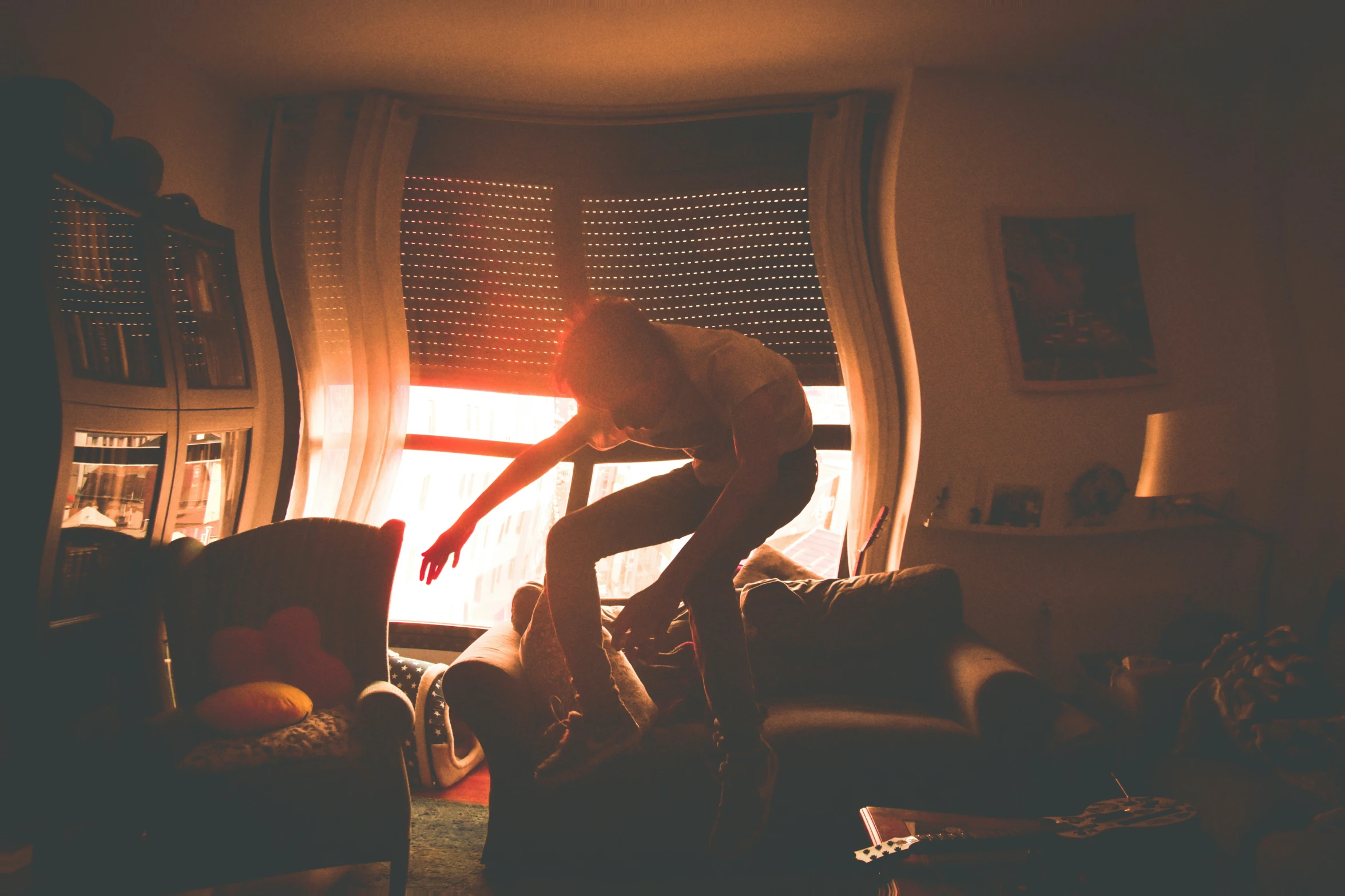 a person jumping over a couch in front of a window