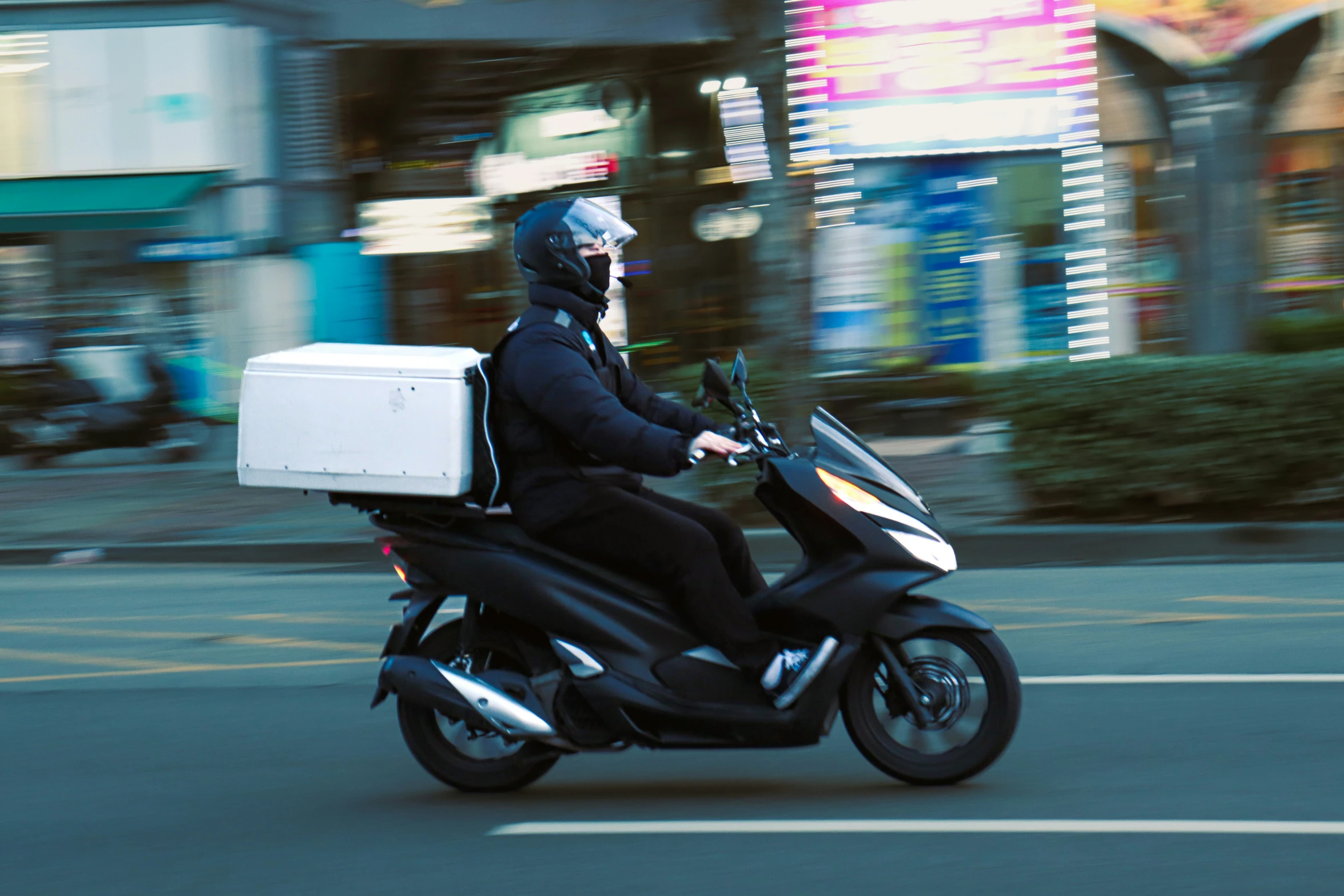 a person with a pizza box on their shoulder rides a moped